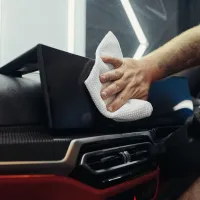 A hand wipes the dashboard of a car with a white cloth, inside a modern vehicle, indicating cleaning or maintenance.
