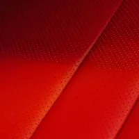 Red leather upholstery with evenly spaced perforations, shown in a close-up view. The perforated pattern varies in density across the surface.