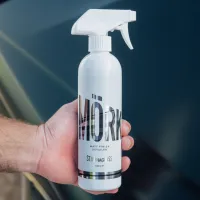 A hand holds a white spray bottle labeled "MÖRK Matt Finish Detailer STJÄRNAGLOSS 500ml" against a dark glossy surface of a vehicle.