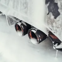 Twin exhaust pipes covered in soapy foam during a car wash, attached to a vehicle with a white foamy exterior.