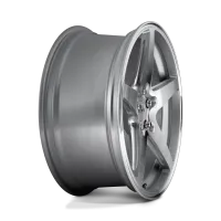 A silver, five-spoke alloy wheel with a polished finish lies against a neutral gray background. The wheel features a central hub with visible lug nut holes and slight reflections on its surface.
