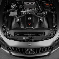 Engine compartment of a sleek, silver Mercedes-Benz sports car, displayed with an open hood in a dimly lit garage.