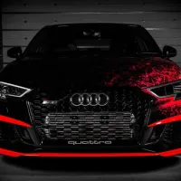 A black Audi car with red accents has a bold front grille displaying the Audi logo and "quattro" text, parked in a dimly lit garage with a closed metallic background.