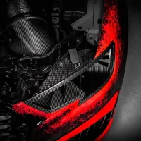 A car engine with carbon fiber components is visible under a partially removed hood in a dark environment, highlighted by striking red accents on the surrounding parts.
