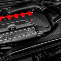 A car engine, with "TFSI" and Audi's four-ring logo on it, features black and carbon fiber components and red accents. The surrounding area includes various engine components and wiring.
