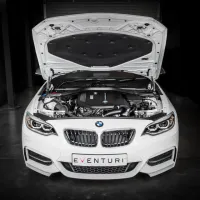White BMW car sits with its hood open, exposing the engine, in a dimly lit garage. A license plate reads "EVENTURI."
