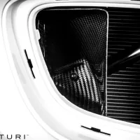 Carbon fiber car engine component in a white vehicle's engine bay with branding "Eventuri" in the bottom left corner. Various parts and textures are visible in a tightly framed shot.
