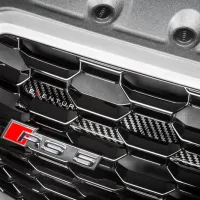 The front grille of a car displays a badge reading "RS 5." Honeycomb pattern design with some carbon fiber accents; text "EVENTURI" visible on one of the hexagons.
