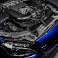 A high-performance car engine with advanced carbon-fiber components is exposed in a blue vehicle parked on a concrete surface.