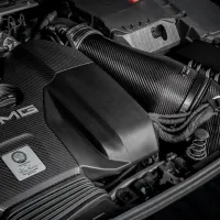 A carbon-fiber-clad AMG engine sits within a car’s engine bay. On it is a metallic emblem with the text, “Handcrafted by Tobias Rommel, Affalterbach, Germany,” highlighting its handcrafted nature.