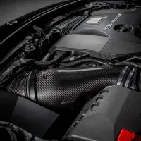 The image shows a high-performance car engine with "AMG" branding, featuring prominent carbon fiber components and intricate wiring, situated within a well-organized engine bay.
