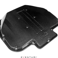 Black carbon fiber car engine cover with visible mounting screws and textured surface, lying on a white background. Text below reads "EVENTURI™."