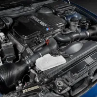 A high-performance BMW engine with a carbon fiber cover and various components visible, situated inside a car’s engine bay. "BMW POWER" is written on the engine cover.