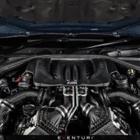 High-performance car engine with twin air intake pipes sits within an open hood, featuring the "M" logo and surrounded by metallic components. Text at the bottom reads: "EVENTURI".