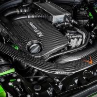 Carbon fiber-covered engine with “M Power” text displayed amidst various components and bright green accents in the surrounding car body, suggesting a high-performance vehicle.