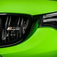 Close-up of a vibrant green car's front end; featuring a chrome grille with "M3" badge and sleek, modern headlight design against a black background.