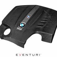 Carbon-fiber engine cover with BMW logo and M stripes inlay, resting isolated on white background. Text: "POWERED BY M" and "EVENTURI" at the bottom.
