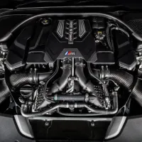A high-performance engine with multiple carbon fiber components and visible intake manifolds; text reads "BMW M Power". The engine is mounted inside a car's engine bay.
