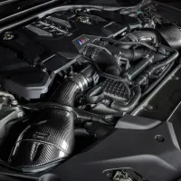 A high-performance engine with carbon fiber components is installed in a car's engine bay, displaying intricate black and silver parts with precision engineering details.
