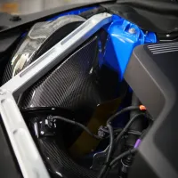 A section of a car engine bay featuring carbon fiber parts, blue and black components, and metal brackets with various wires connected, highlighting the complex mechanical structure.