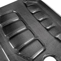 A black, carbon fiber engine cover featuring multiple raised geometric patterns. The background is white, highlighting the shiny, textured surface of the cover.