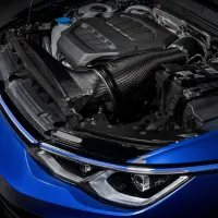 A car engine with various components is exposed under an upraised hood, revealing a large carbon-fiber air intake system, battery, and other parts within a blue, modern vehicle.