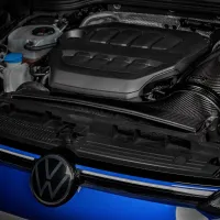 A Volkswagen car engine with visible components like the air filter, coolant reservoir, and engine cover, is installed under an open hood, located in a garage or workshop setting.