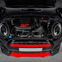 A car with an open hood displays a compact engine labeled "GP" in red, featuring prominent headlights and red accents, situated in a well-lit garage setting.