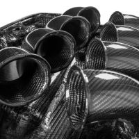 Glossy black carbon fiber intake trumpets are arranged close together, nestled within a molded carbon fiber base, reflecting studio lights.
