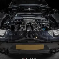 A car with the engine compartment exposed is showcasing its high-performance parts under bright lighting in a dimly lit garage. Text present: "EVENTURI".