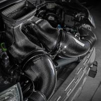 Carbon fiber air intake installed inside a car engine bay, featuring smooth, sculpted designs and labeled "Eventuri." The car’s front bumper and adjacent engine components are visible in a dimly lit garage setting.