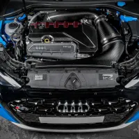 A car engine with "Audi TFSI" branding and red accents is installed under the open hood of a blue vehicle, with surrounding components and cables visible.