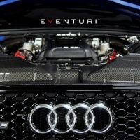 The blue Audi RS 5 showcases its exposed engine with "Eventuri" branding above, surrounded by carbon fiber components and the iconic Audi grille in a dimly lit setting.