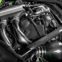 A car engine with intricate braided carbon fiber hoses and components. The context is under the hood of a vehicle highlighted with green accents on the edges.