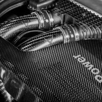Carbon fiber tubes connected to an engine covered by a carbon fiber panel inscribed with "M Power" in an automotive engine bay.