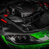 A high-performance car's engine bay, featuring a carbon fiber engine cover with "Eventuri" branding, surrounded by black and red components, and a green, geometric-patterned front body.
