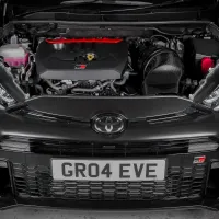 Car with open hood displaying engine components, situated in a dimly lit garage. The front grille has a license plate reading "GR04 EVE" and a Toyota emblem.