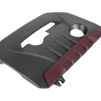 A carbon fiber engine cover with a rectangular cutout and circular hole, featuring a textured surface and red-striped section on its right side, isolated on a white background.