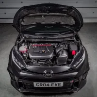 A car with its hood open displays the engine bay and components in a garage. The license plate reads: GR04 EVE.