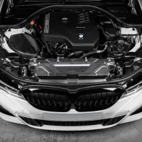 BMW car engine with visible branding, situated under an opened hood, in a clean, white car body, viewed from the front in an indoor setting. Text: "BMW" and "TwinPower Turbo."