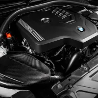 An engine with a black cover marked "BMW" and "TwinPower Turbo" is housed in a car's engine bay, surrounded by various mechanical components and tubing.