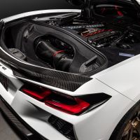 A white car with the rear hood open revealing a detailed engine compartment, featuring carbon fiber and red accents, in a studio setting. "CORVETTE" text is visible on the rear bumper.