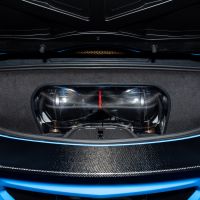 Carbon fiber air intake, enclosed in a clear casing, sits inside the trunk of a high-performance car with visible blue bodywork and black interior lining.