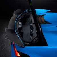 A blue sports car's rear hatchback is open, revealing a spacious trunk with carbon fiber detailing, under dark ambient lighting. The left rear taillight is visible.