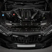 Car engine compartment (object) displayed in an open hood (action) of a black BMW vehicle, featuring carbon fiber components and the "M" logo on the central cover (context).