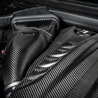Carbon fiber engine components showcased in an intricately designed vehicle engine bay, illuminated under strong lighting, revealing the texture and detail of the carbon fiber material.
