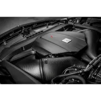 A sleek, black carbon fiber car engine cover with a red arrow and a silver emblem installed in a high-performance engine bay, surrounded by various engine components and hoses.