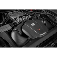 A carbon fiber engine cover with a red arrow, labeled "V10 TFSI", housed in a high-performance car's engine bay, surrounded by various metallic and plastic components.