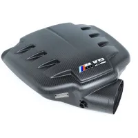 Black carbon fiber engine cover featuring a vented design, an “M V8” badge, and a metal plaque with text, positioned against a white background.