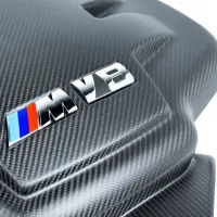 Carbon fiber car engine cover with a glossy "M V8" emblem featuring blue and red stripes, suggesting high-performance, situated in a well-lit environment.
